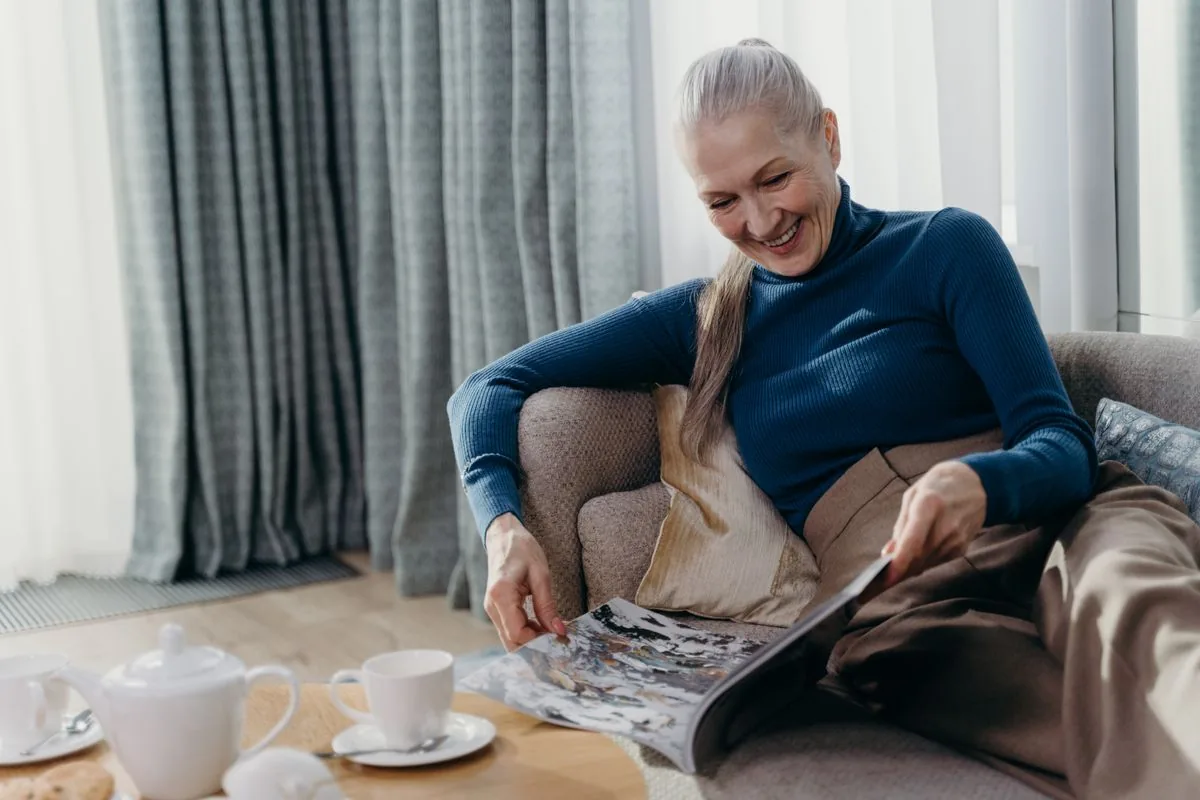 Une lectrice souriante feuillette un magazine dans son salon