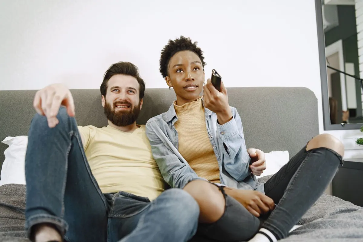 Un couple installé sur un canapé choisit un programme avec une télécommande