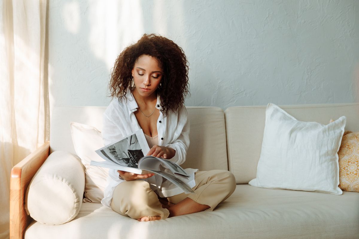 Une femme lit un magazine sur un canapé dans un salon lumineux