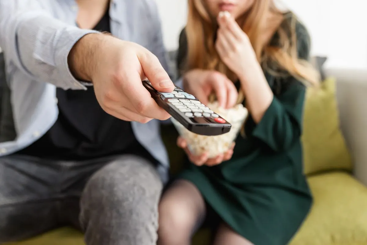 Une télécommande au premier plan devant un couple installé sur un canapé